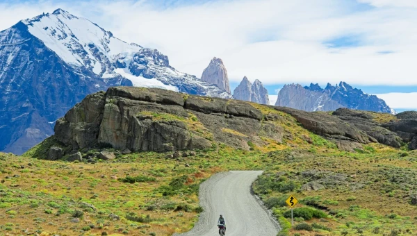 February picture. A cyclist riding on a gravel road through Torres del Paine National Park with a utterly beautiful mountain range in the background.