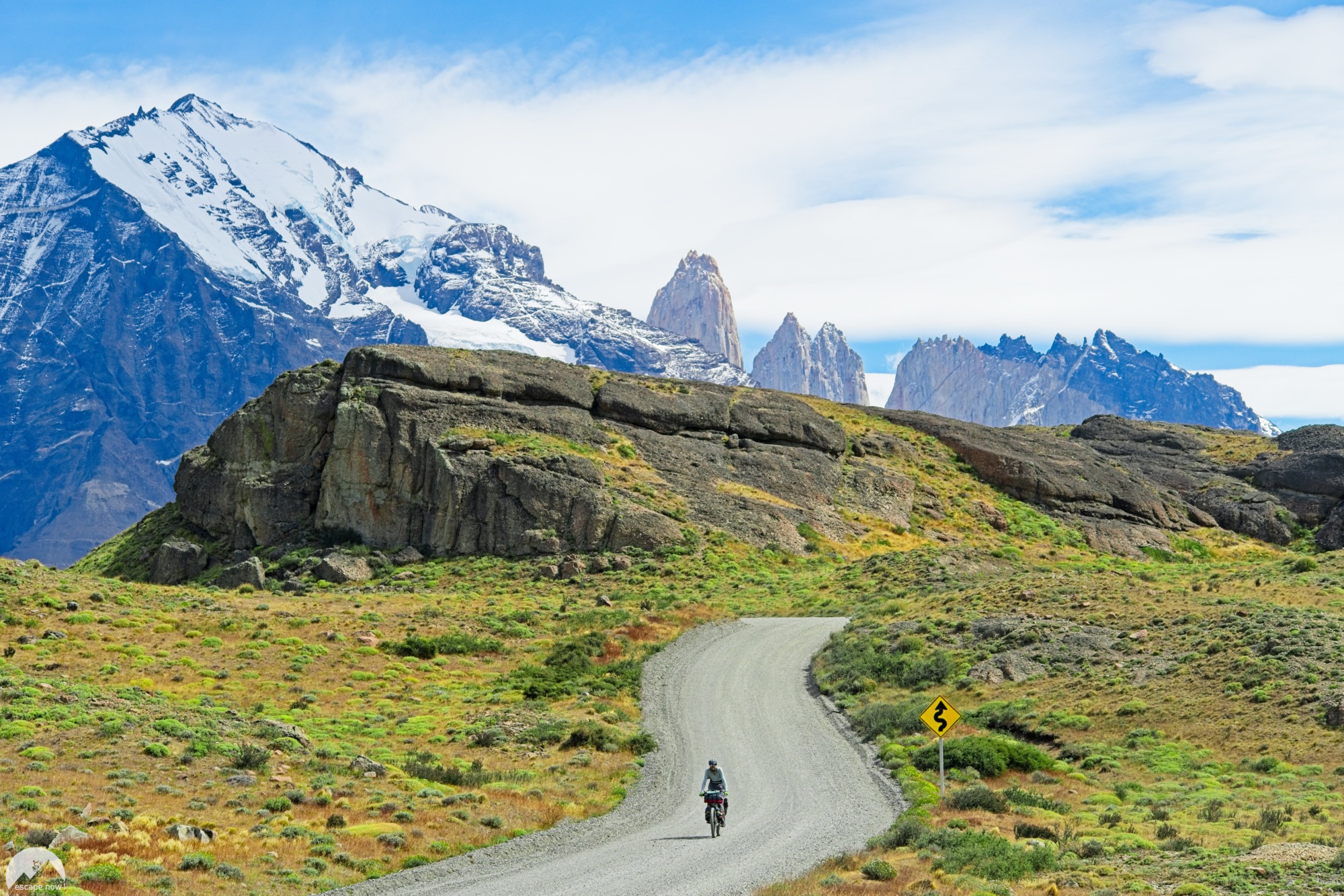 February picture. A cyclist riding on a gravel road through Torres del Paine National Park with a utterly beautiful mountain range in the background.
